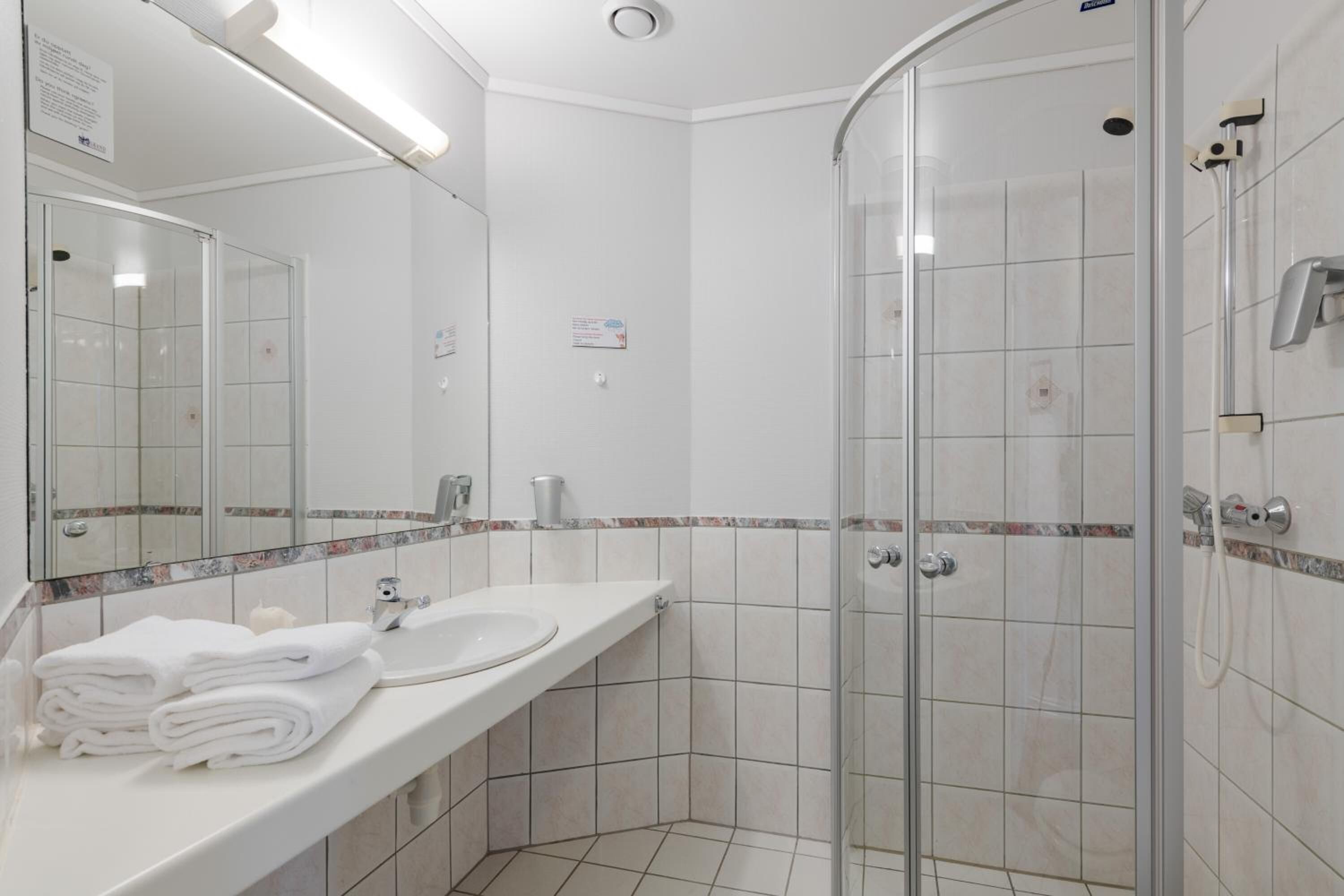 Un baño moderno con ducha de vidrio, un lavamanos blanco y un espejo sobre él.