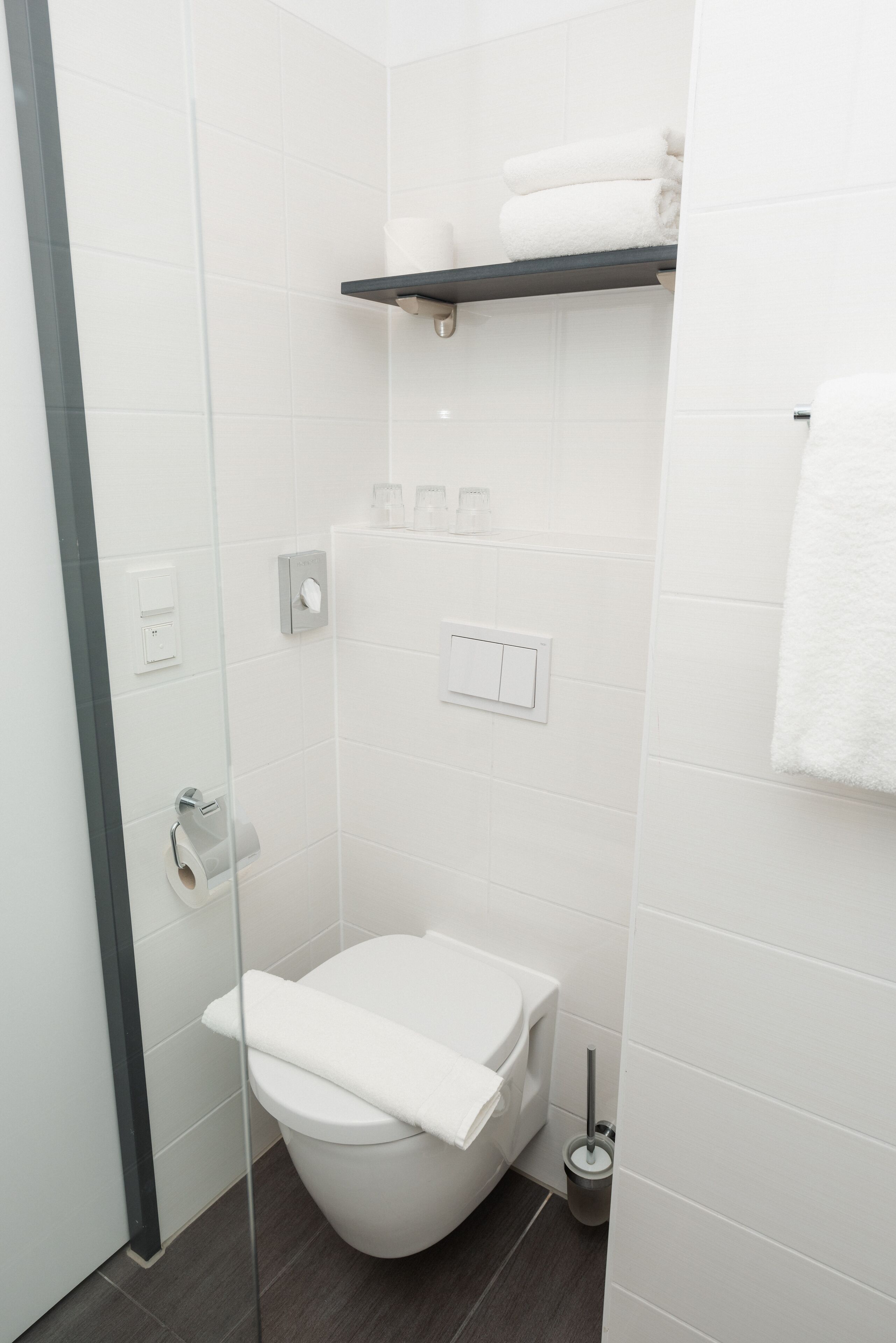 Un baño moderno con cabina de ducha de vidrio, inodoro blanco y un estante con toallas.