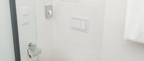 Un baño moderno con cabina de ducha de vidrio, inodoro blanco y un estante con toallas.