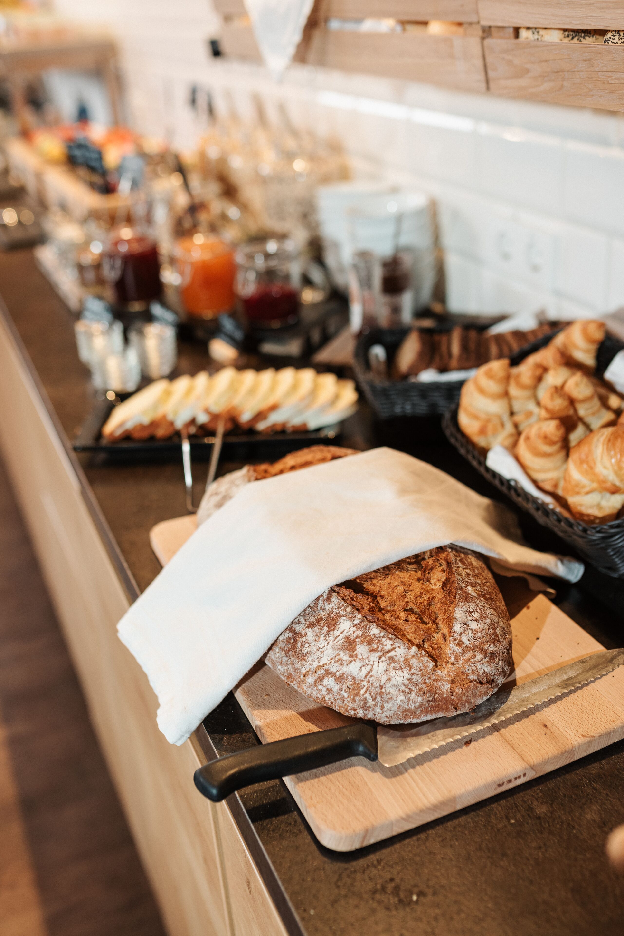 A breakfast buffet with various pastries and bread, including a loaf of bread on a cutting board.