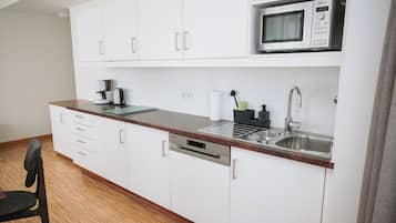 A compact kitchen with white cabinets, a stainless steel sink, a microwave, and a coffee maker.