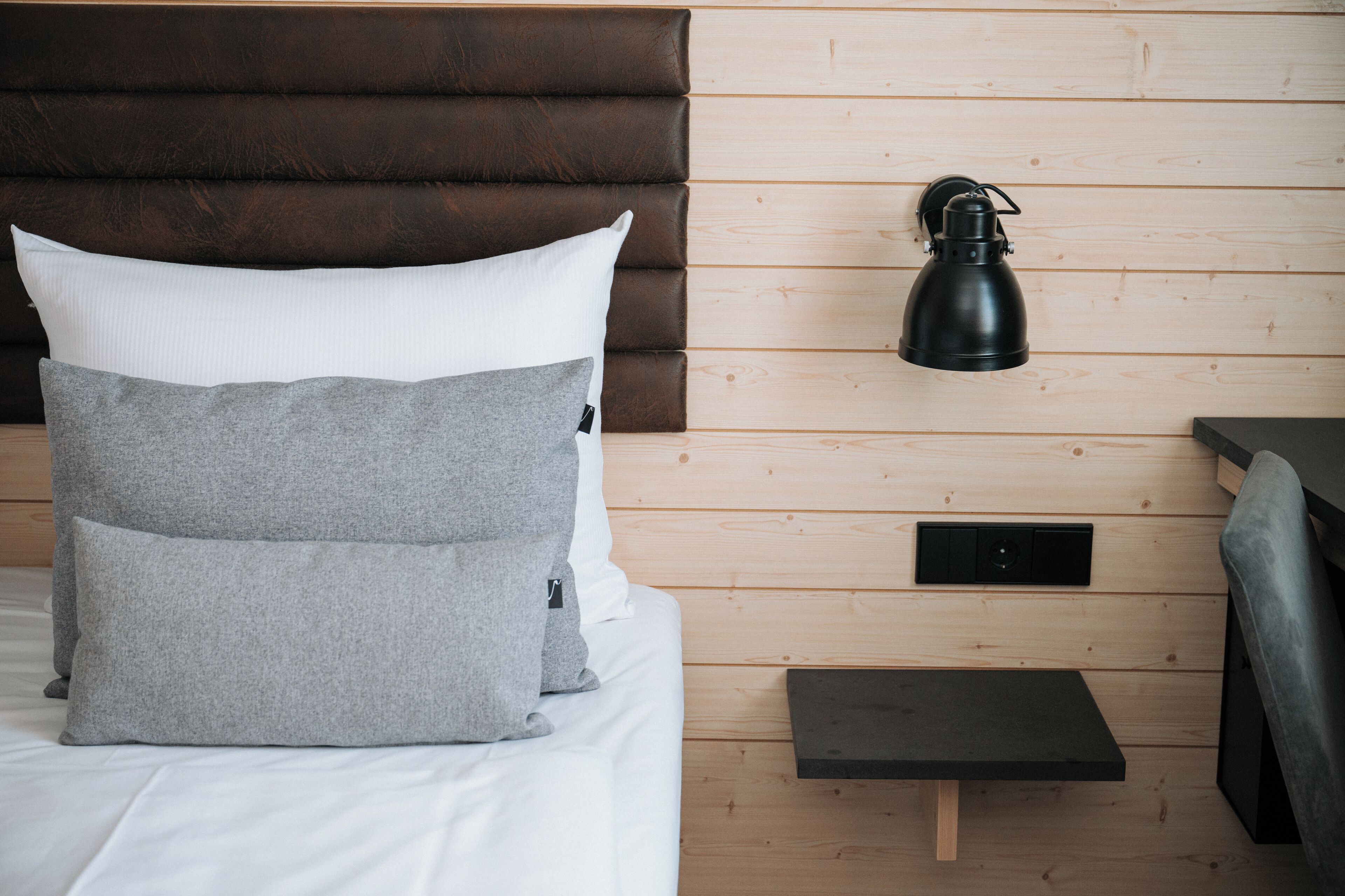 A bed with two pillows, a bedside table, a wall-mounted lamp, and a small shelf.