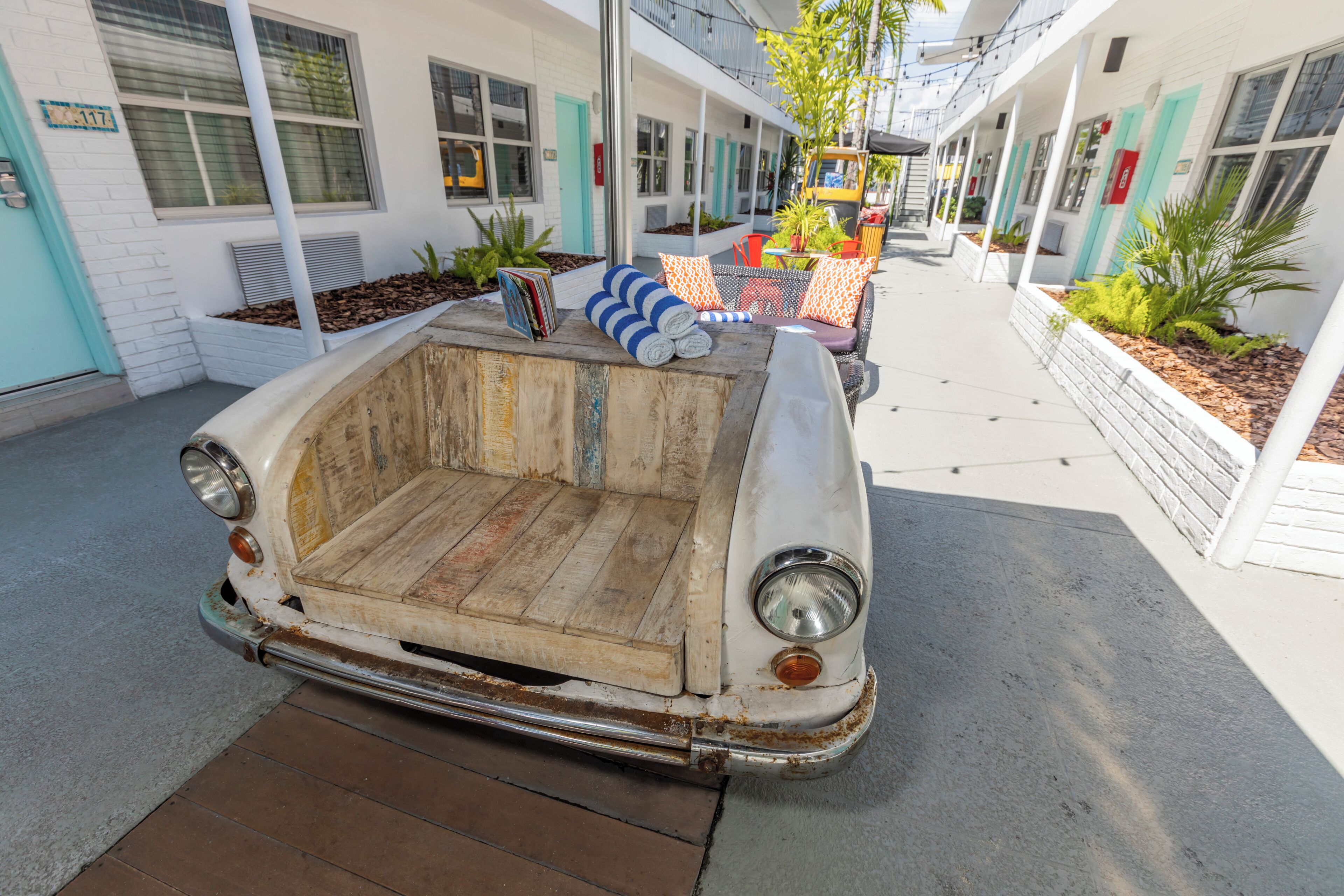 Un coche antiguo convertido en cama en un patio con un edificio blanco y plantas.