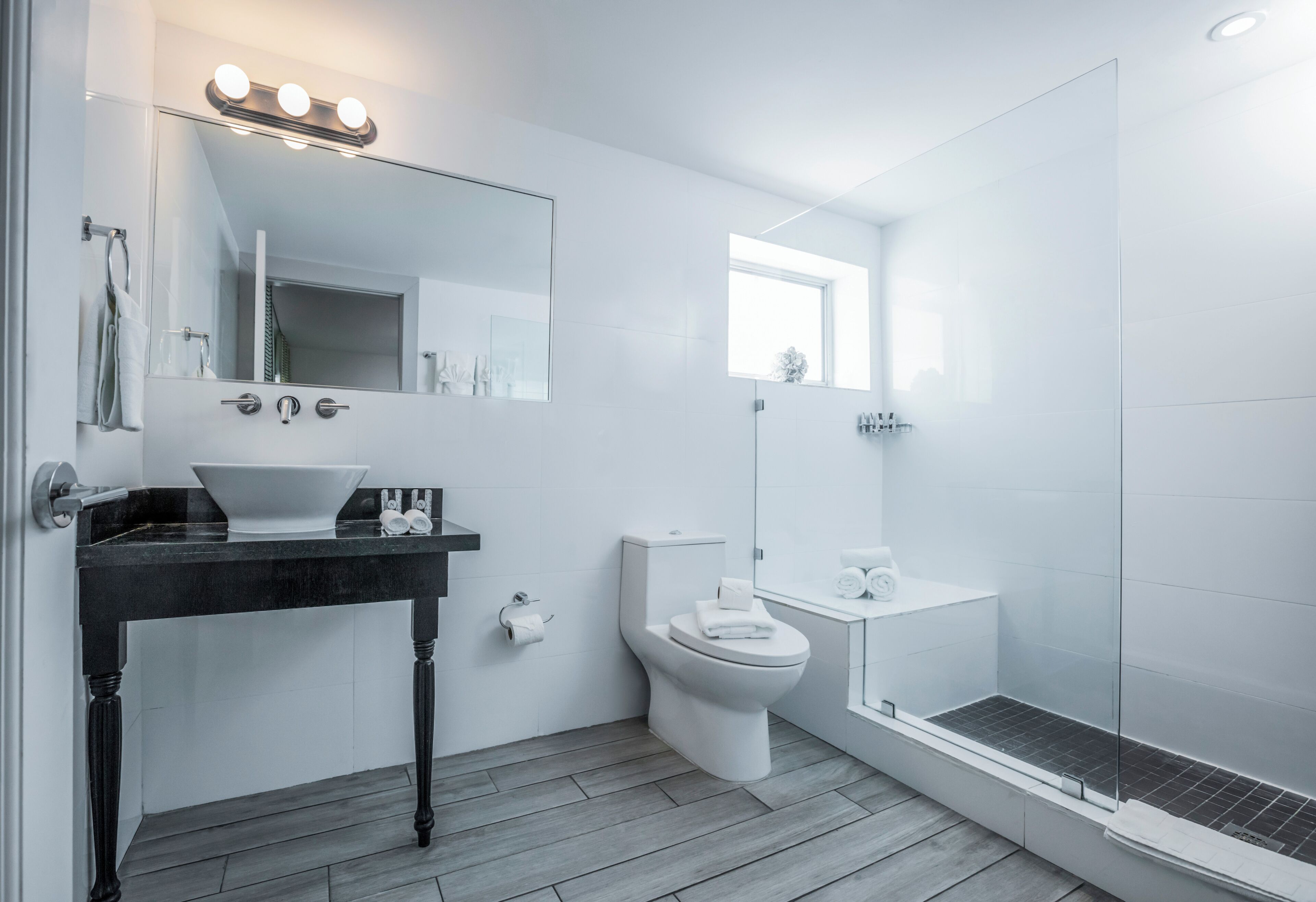 A modern bathroom with a black vanity, white toilet, and a glass shower enclosure.