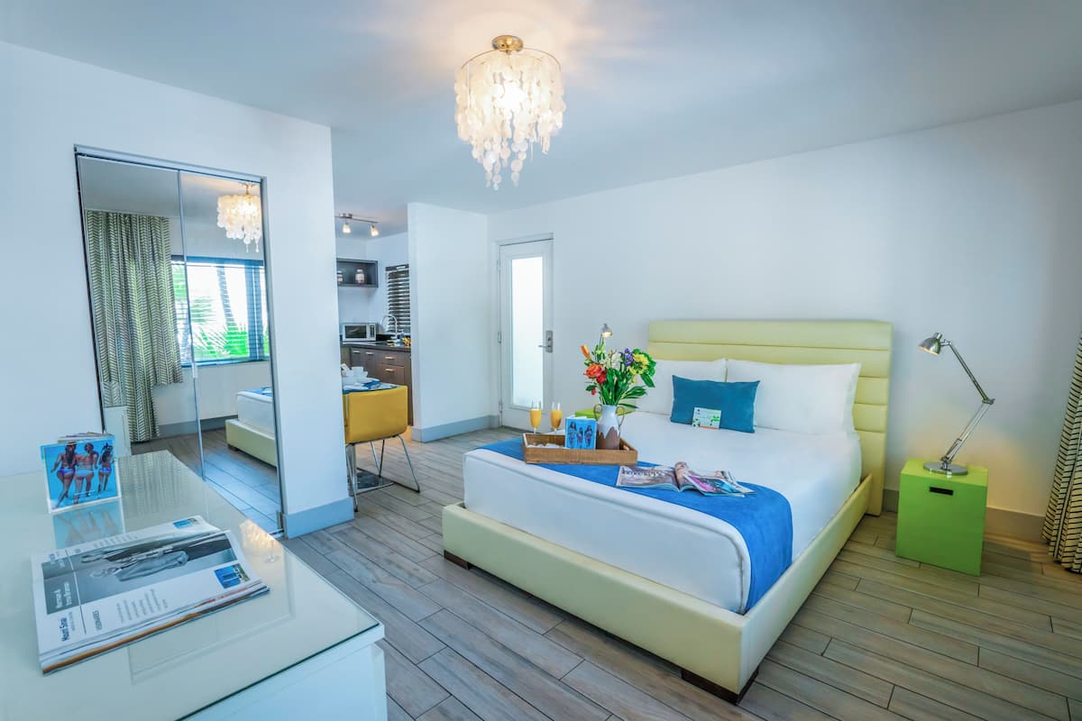 A modern hotel room with a large bed, a glass desk, and a view into the kitchen area.