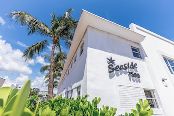 A pool area with a clear blue pool, lounge chairs, umbrellas, and a wooden deck with a fruit tray. at Seaside All Suites Hotel