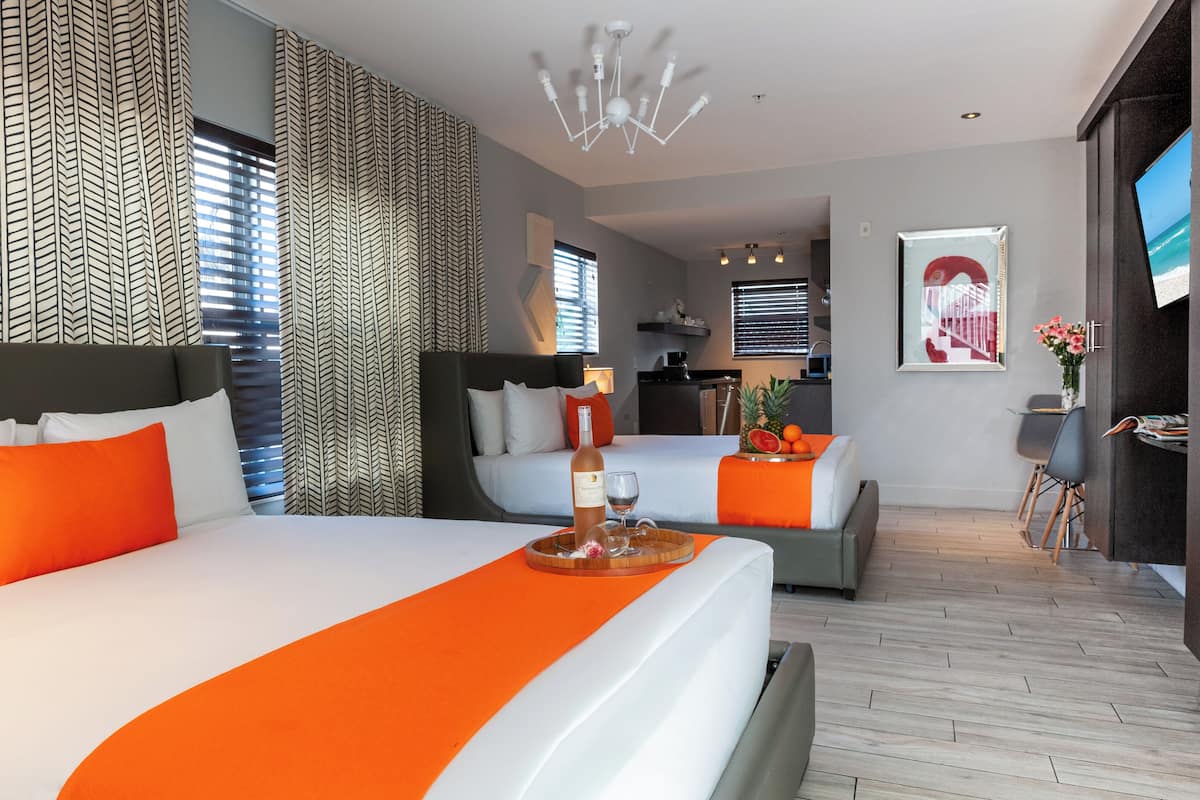 A modern hotel room with a large bed, a dining area, and a kitchen in the background.