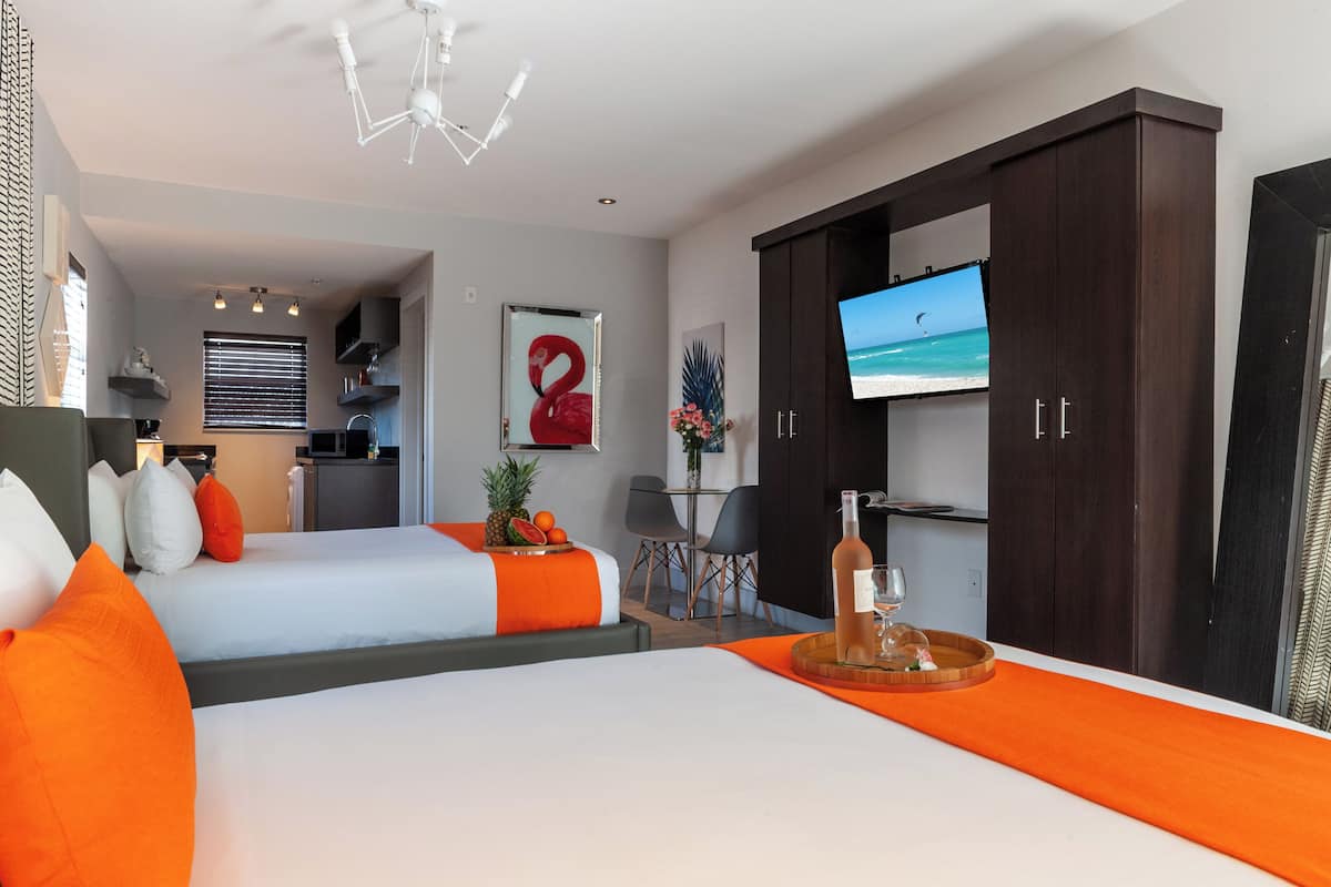 A modern hotel room with two beds, a TV, a minibar, and a view of the beach.