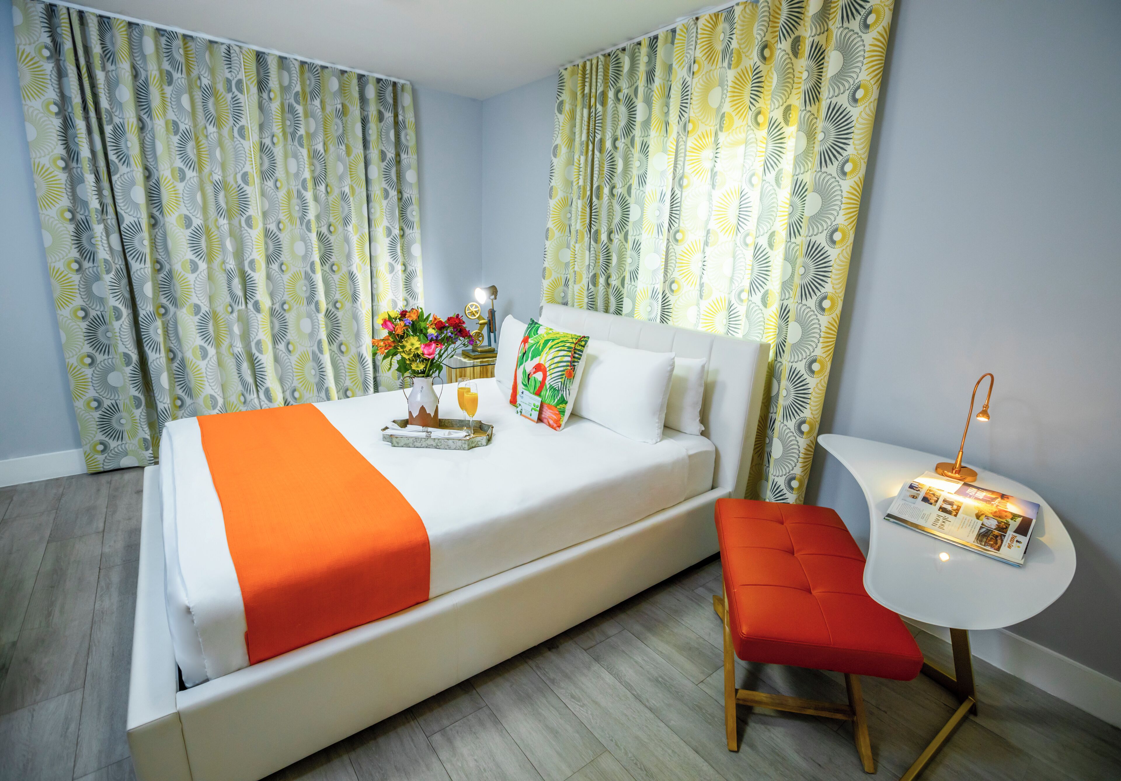 A hotel room with a bed, a small table with a lamp, and a red bench.