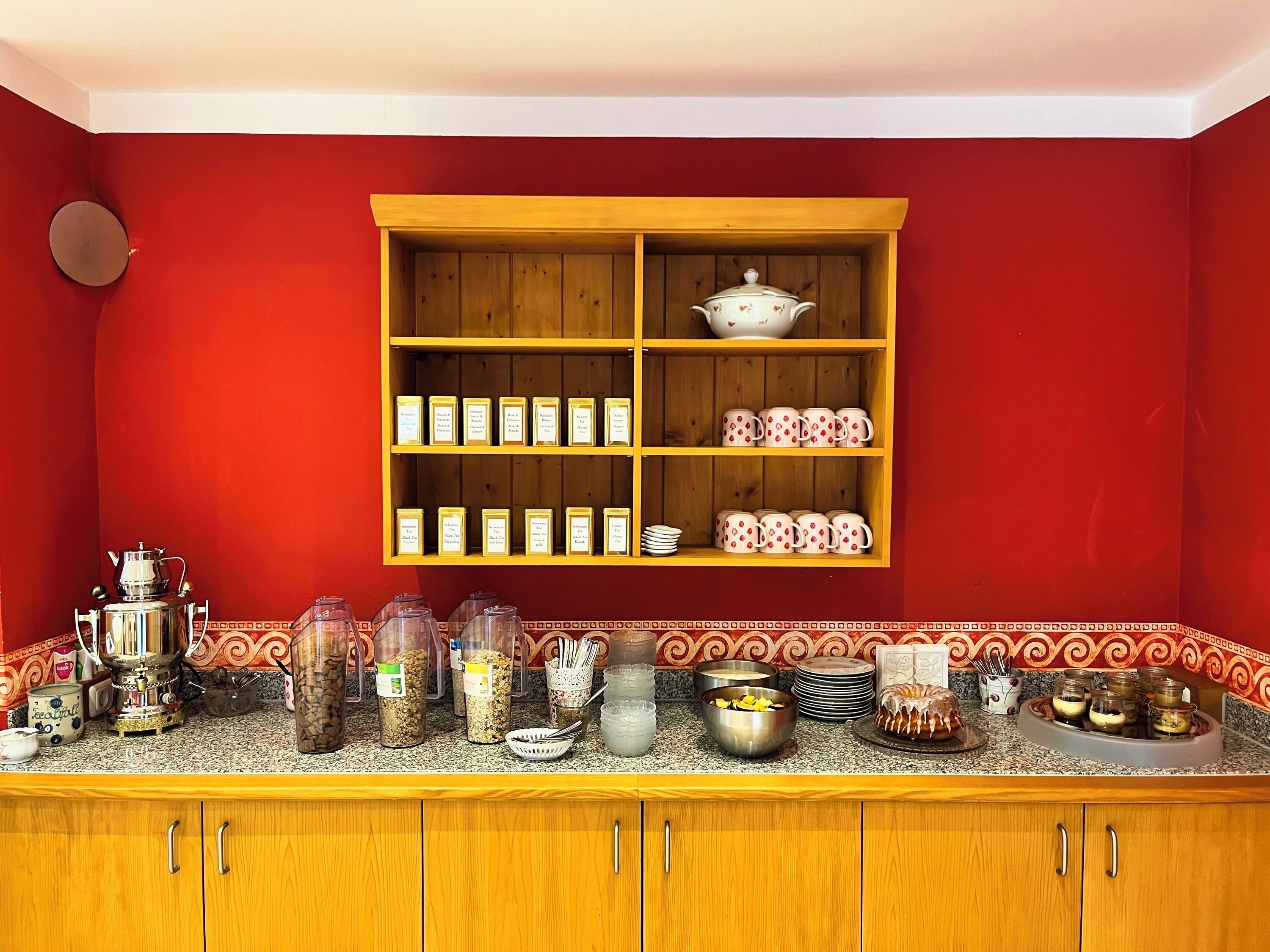 Una cocina con pared roja, armarios de madera, un estante para especias y varios utensilios de cocina.
