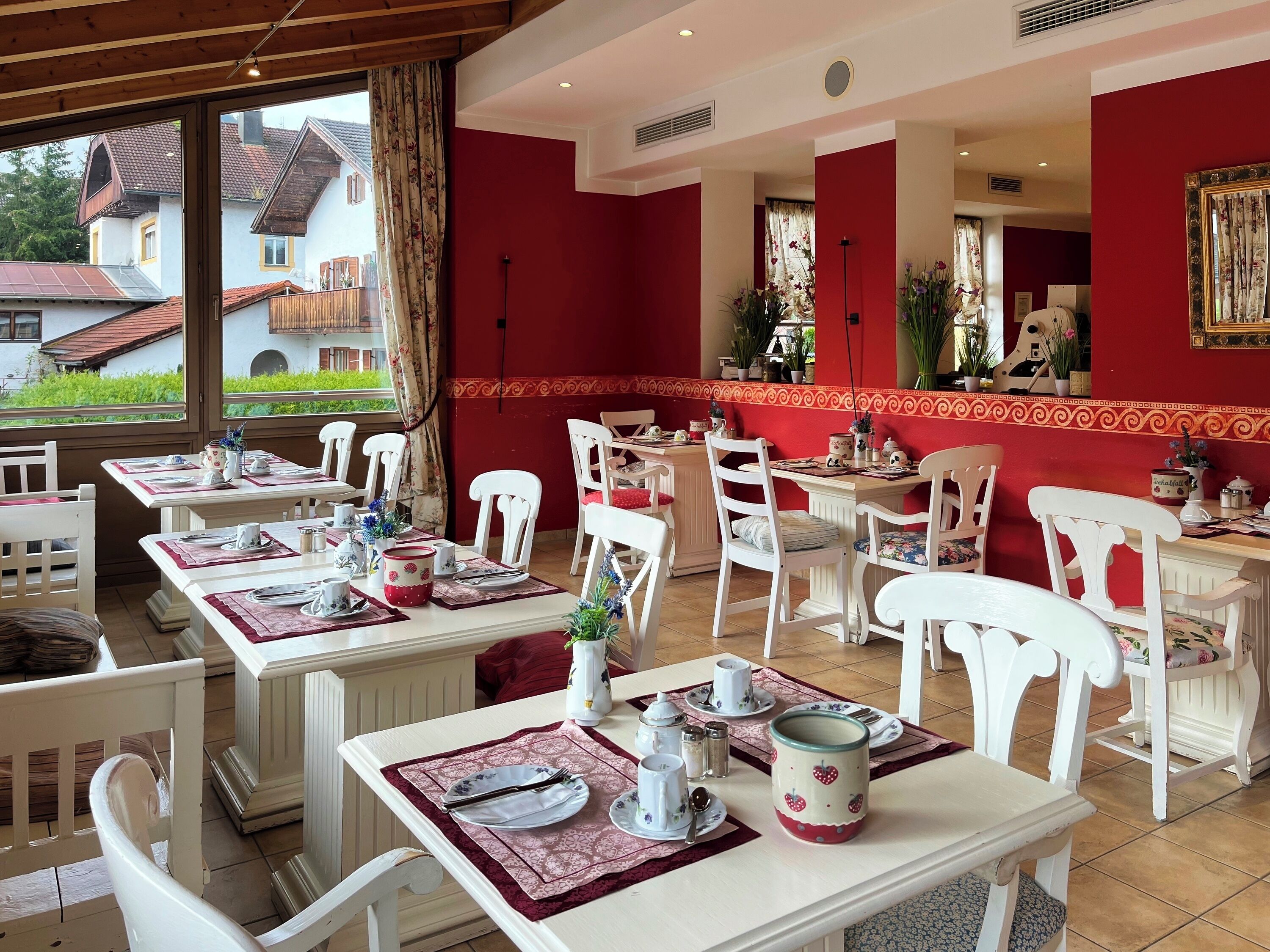 Un espace repas avec des tables disposées pour accueillir quatre personnes, des chaises blanches et un mur d’accent rouge.