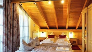 A hotel room with a wooden ceiling, a bed with pillows and towels, bedside lamps, and a window with curtains.