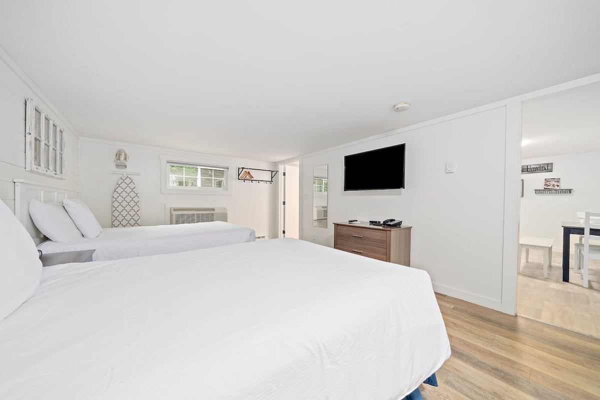 Un dormitorio con dos camas, televisor, cómoda de madera y una mesita.
