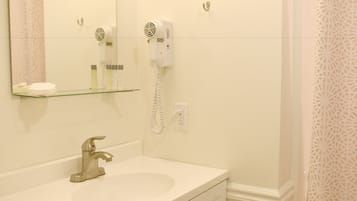 Kylpyhuone, jossa on pesuallas, peili, hiustenkuivaaja ja lasihylly, jossa on hygieniatuotteita.
