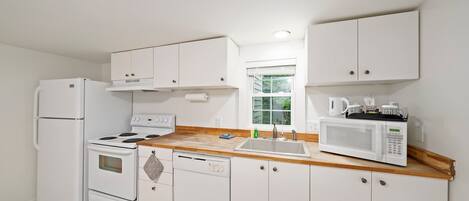 Una cocina compacta con electrodomésticos blancos, encimera de madera y armarios blancos.
