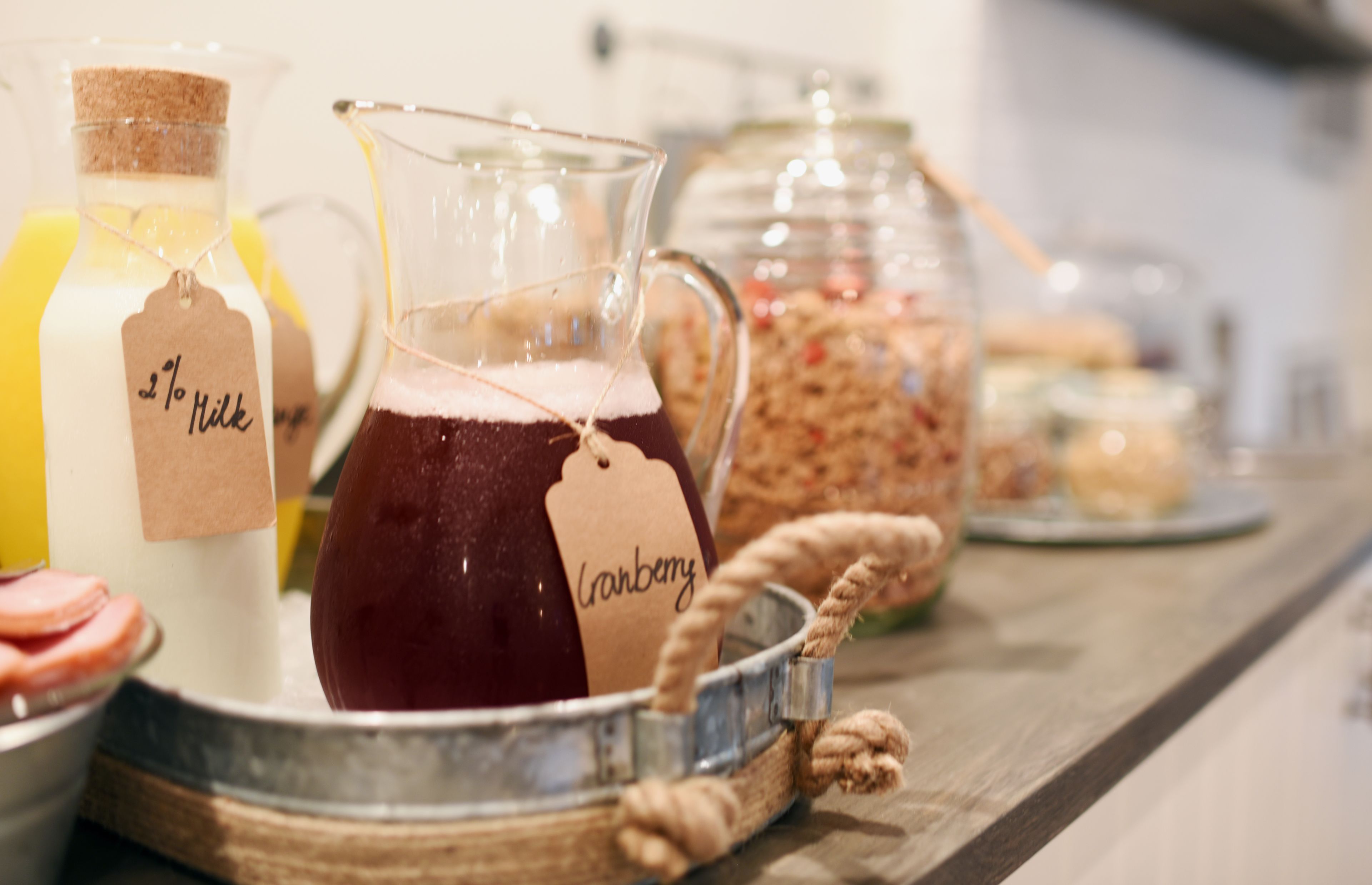 Una bandeja con un jarro de jugo de arándano, una botella de leche y frascos de granola.