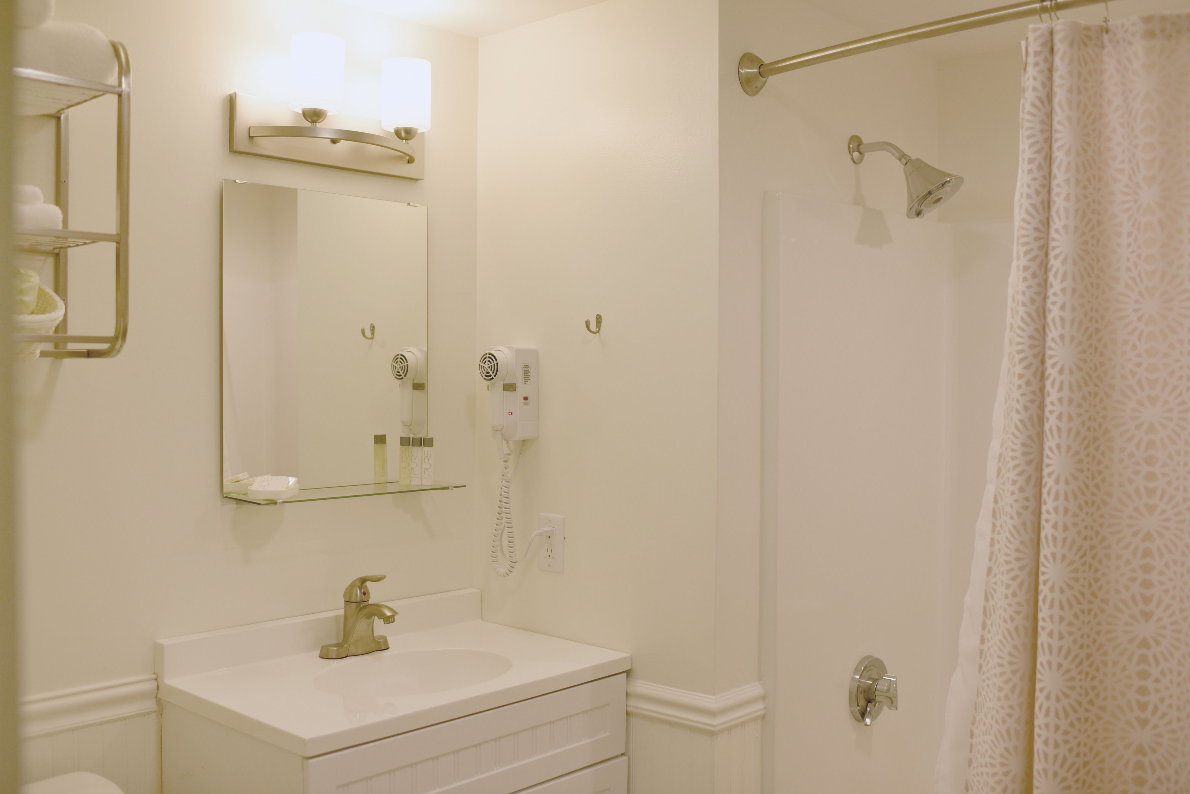 Un baño con lavamanos blanco, espejo y ducha con puerta de cristal.