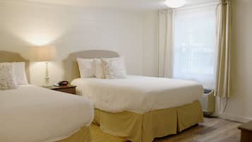 A hotel room with two beds, a bedside table with a lamp, a clock, and a window with curtains.