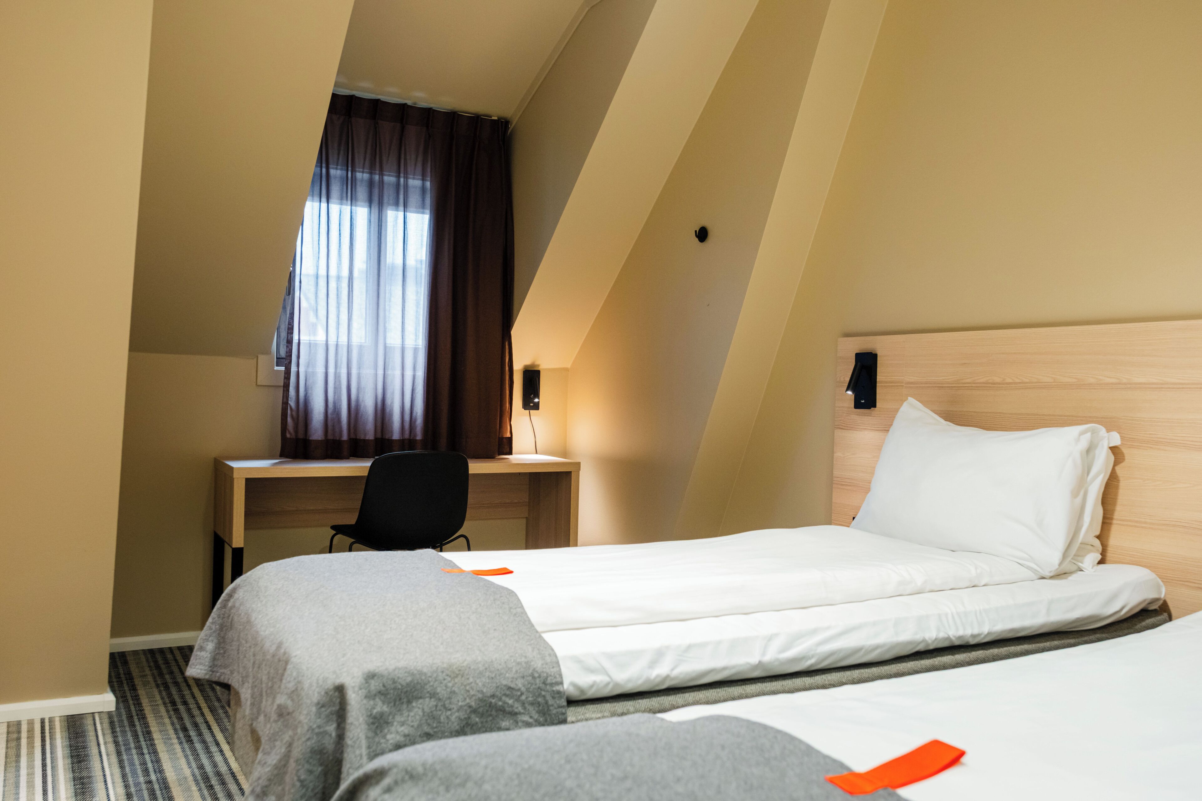 A hotel room with two beds, a desk, a chair, and a window with curtains.