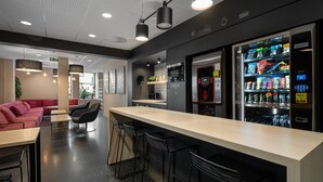 Et moderne barområde med en lang bardisk, sorte barstole, en rød sofa og en automater fyldt med snacks.