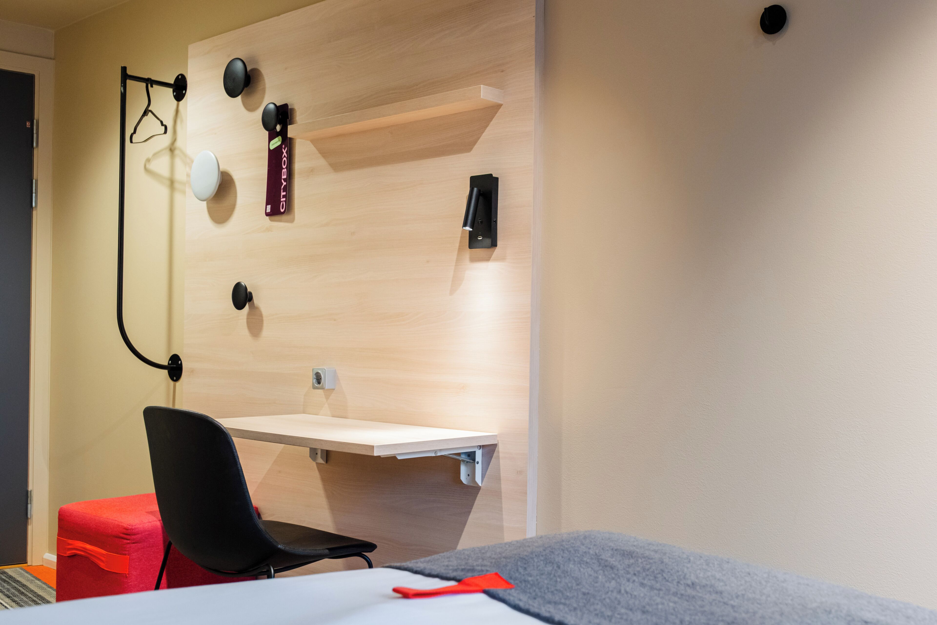A modern room with a wooden accent wall, a desk, a chair, and a red ottoman.