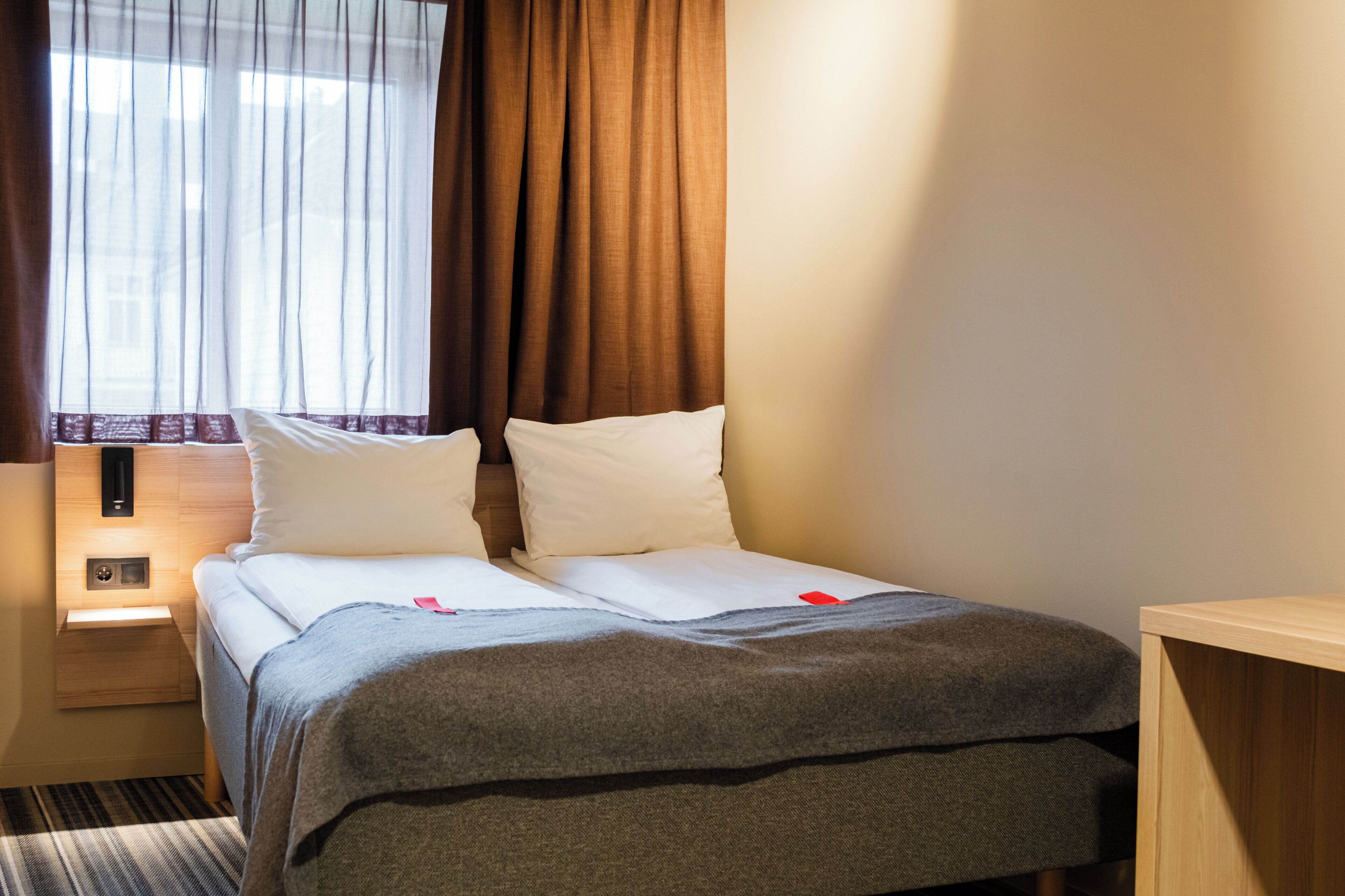 Una habitación de hotel con una cama, una mesita de noche y una ventana con cortinas.