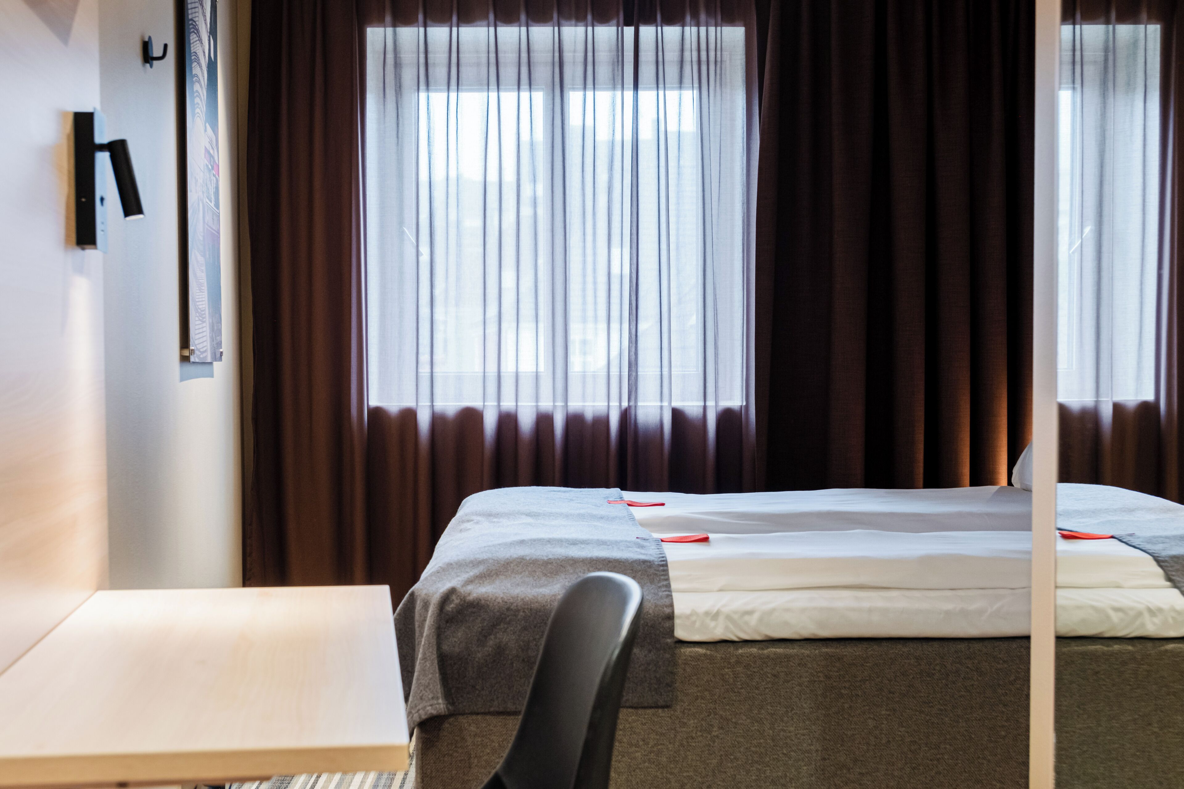 A hotel room with a bed, a desk, and a window with curtains.