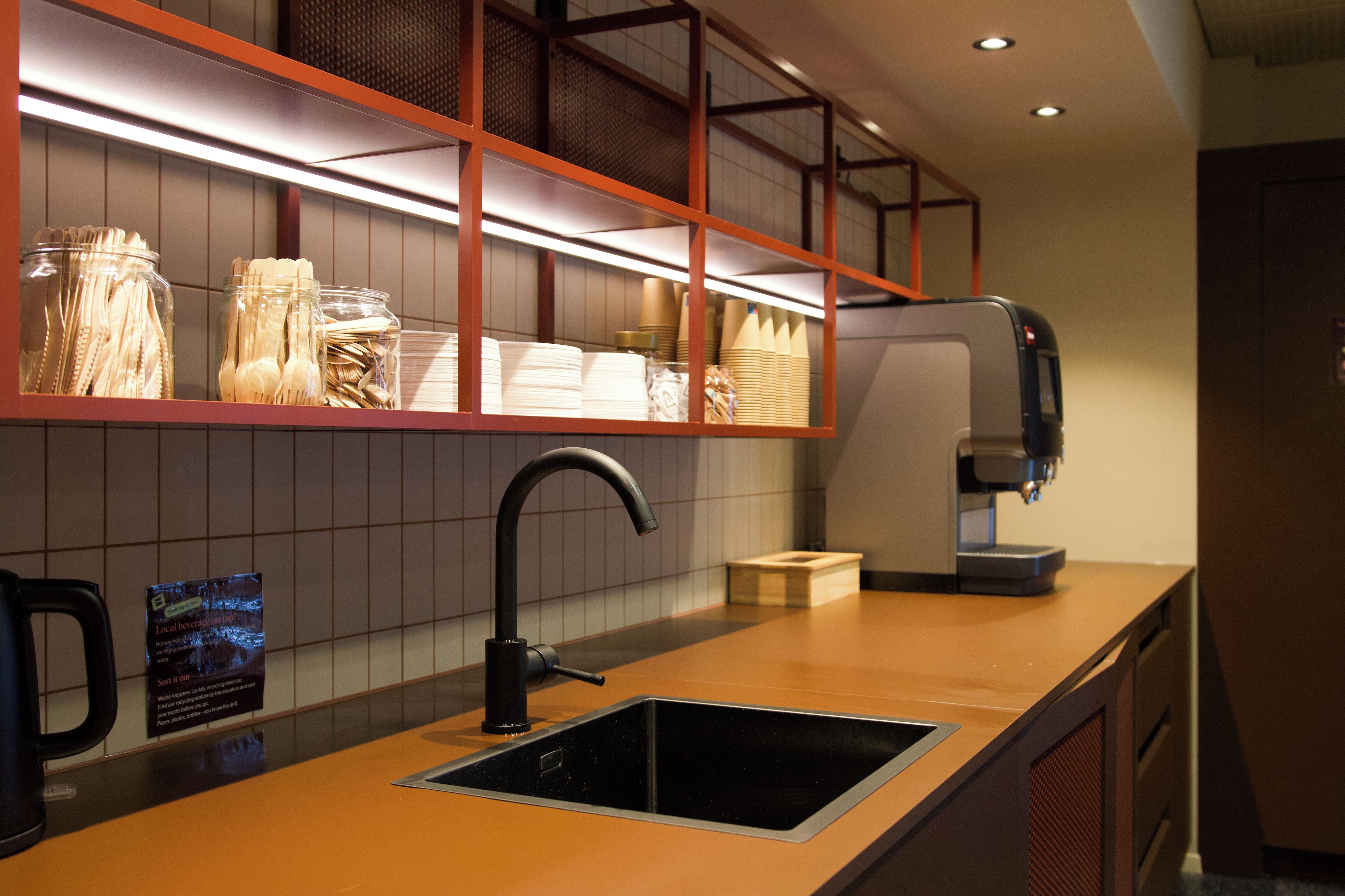 Una cocina moderna con cafetera espresso integrada, un fregadero y estantes con utensilios.