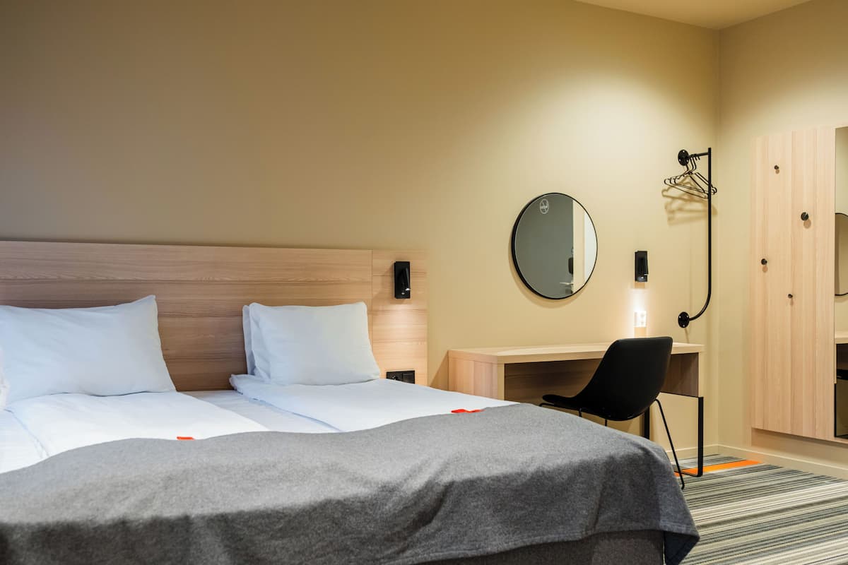 Una habitación de hotel con una cama, un escritorio, una silla, un espejo y un armario.