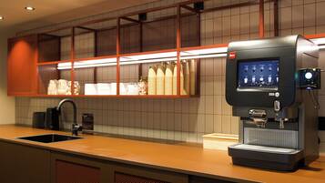 Una cafetera con pantalla digital, un lavamanos y un salpicadero de azulejos.