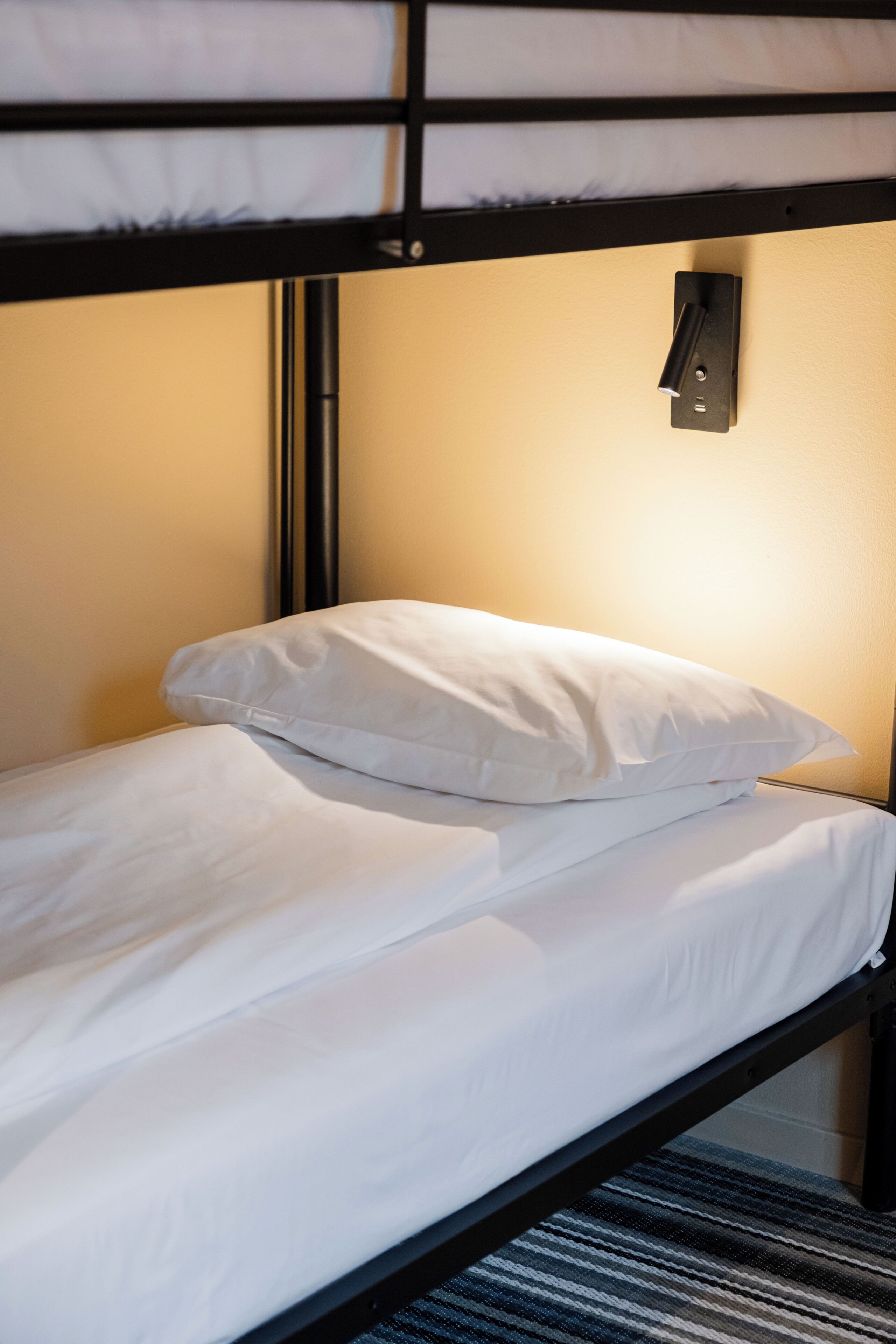 A bunk bed with white bedding and a wall-mounted light fixture.