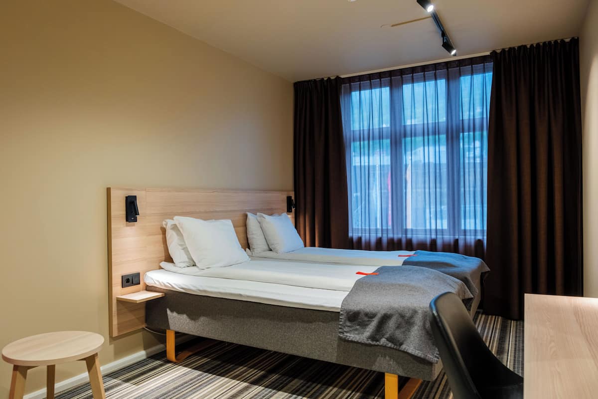 Una habitación de hotel con cama, mesita de noche y un taburete pequeño.