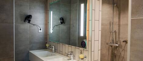 A modern bathroom with two sinks, a large mirror, and a shower.