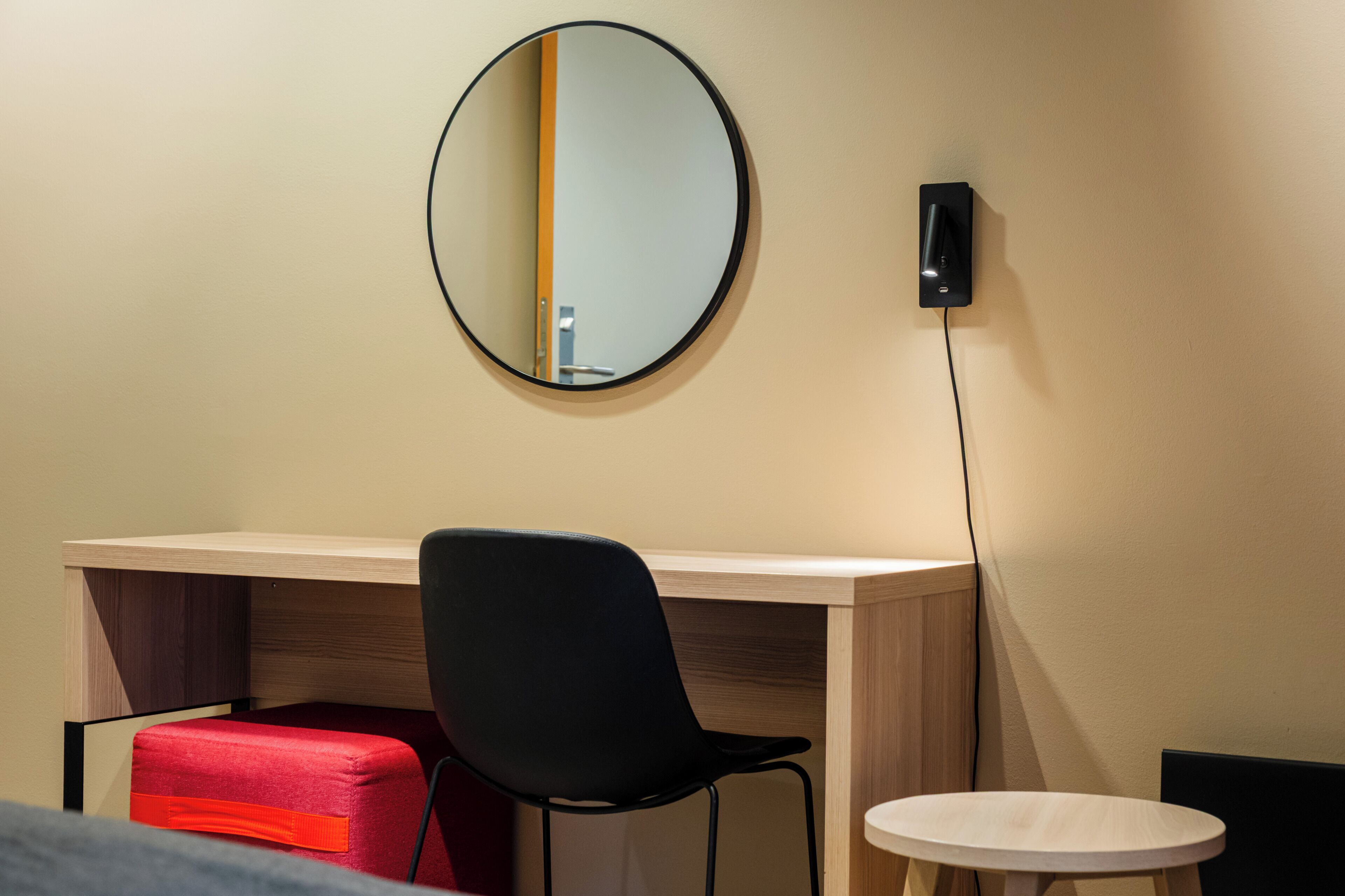 Une pièce comprenant un bureau, une chaise, une petite table ronde et un miroir fixé au mur.