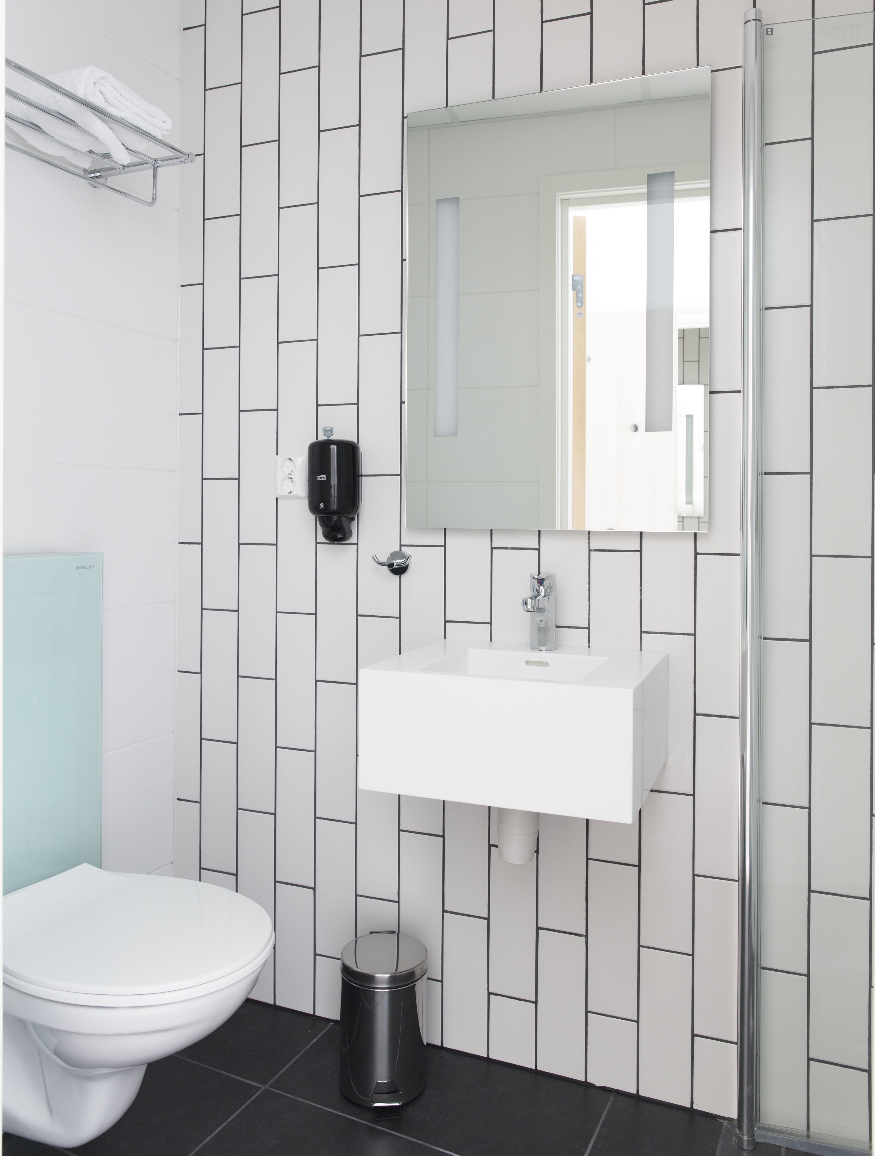 Ein modernes Badezimmer mit einem weißen Waschbecken, einem Spiegel, einer Toilette und einem Mülleimer.