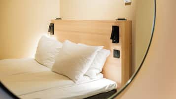 A neatly made bed with white linens and pillows, a wooden headboard, and a wall-mounted thermostat.