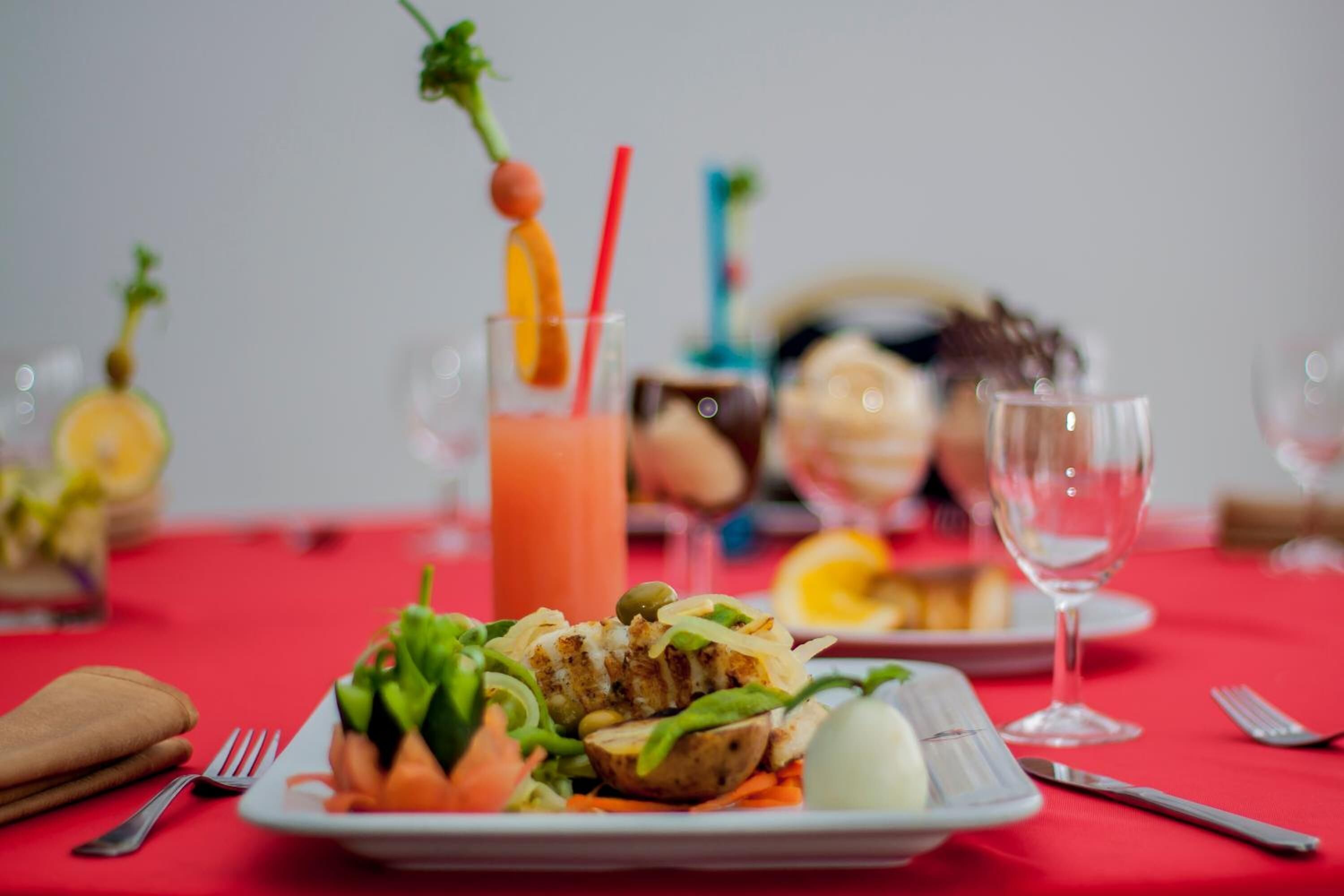 A dining table with a red tablecloth, a plate of food, a glass of drink, and a wine glass.