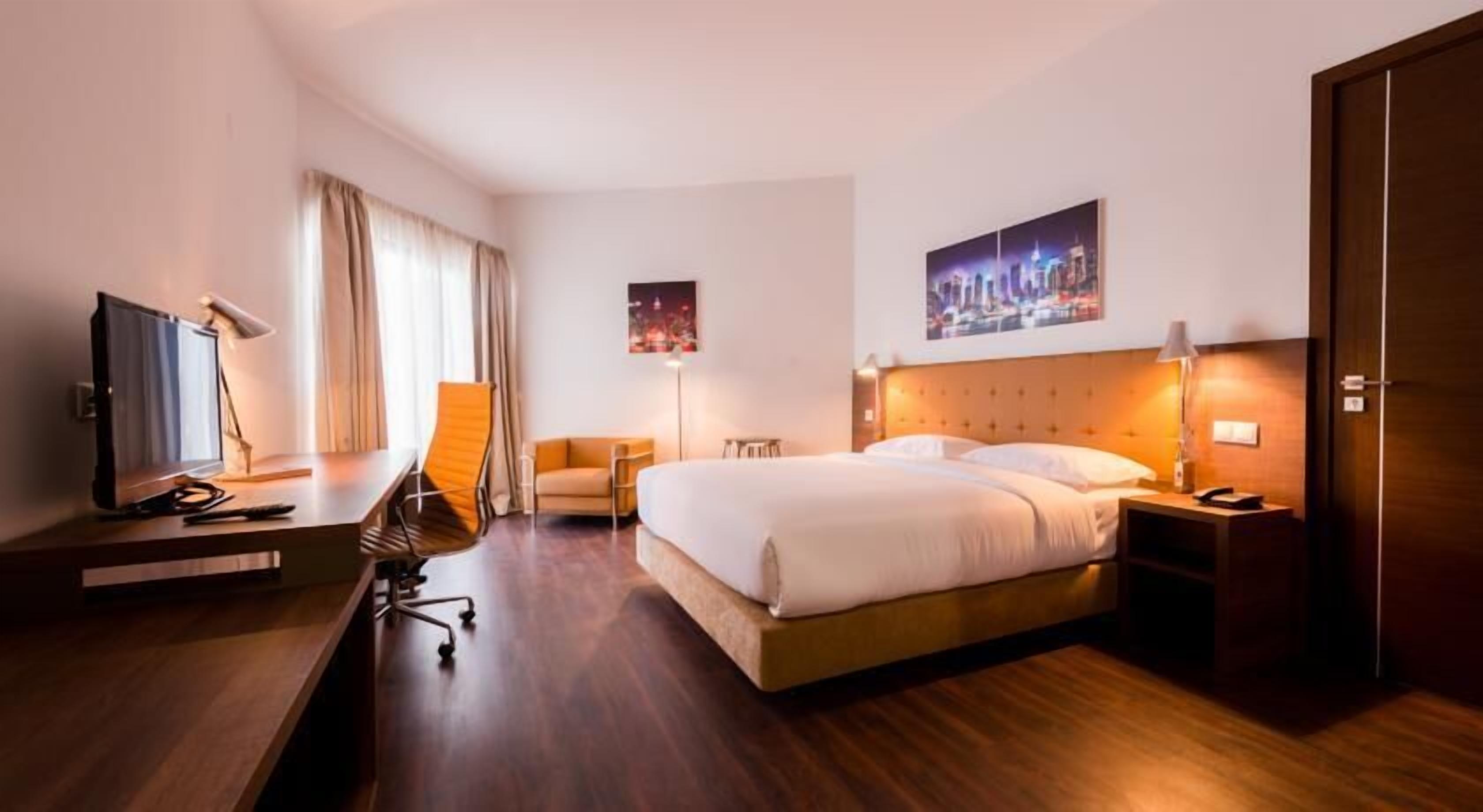 Una habitación de hotel con una cama, un escritorio con computadora, una silla, un televisor y una mesita de noche.