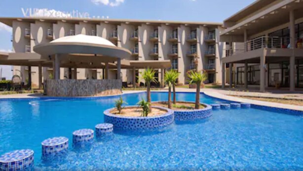 A hotel with a large swimming pool, a covered area, and a building with multiple balconies.