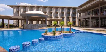 Un hotel con una piscina grande, una zona techada y un edificio con varios balcones.