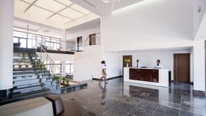 A spacious lobby with a reception desk, a staircase leading to an upper level, and a modern chandelier.