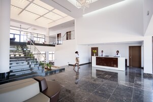 Un vestíbulo amplio con una recepción, una escalera que sube a un nivel superior y un candelabro moderno.