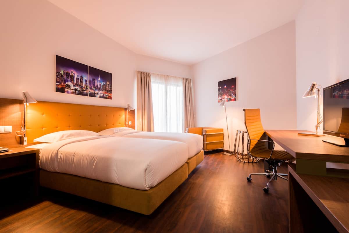 A hotel room with a large bed, a desk, a chair, a TV, and two paintings on the wall.