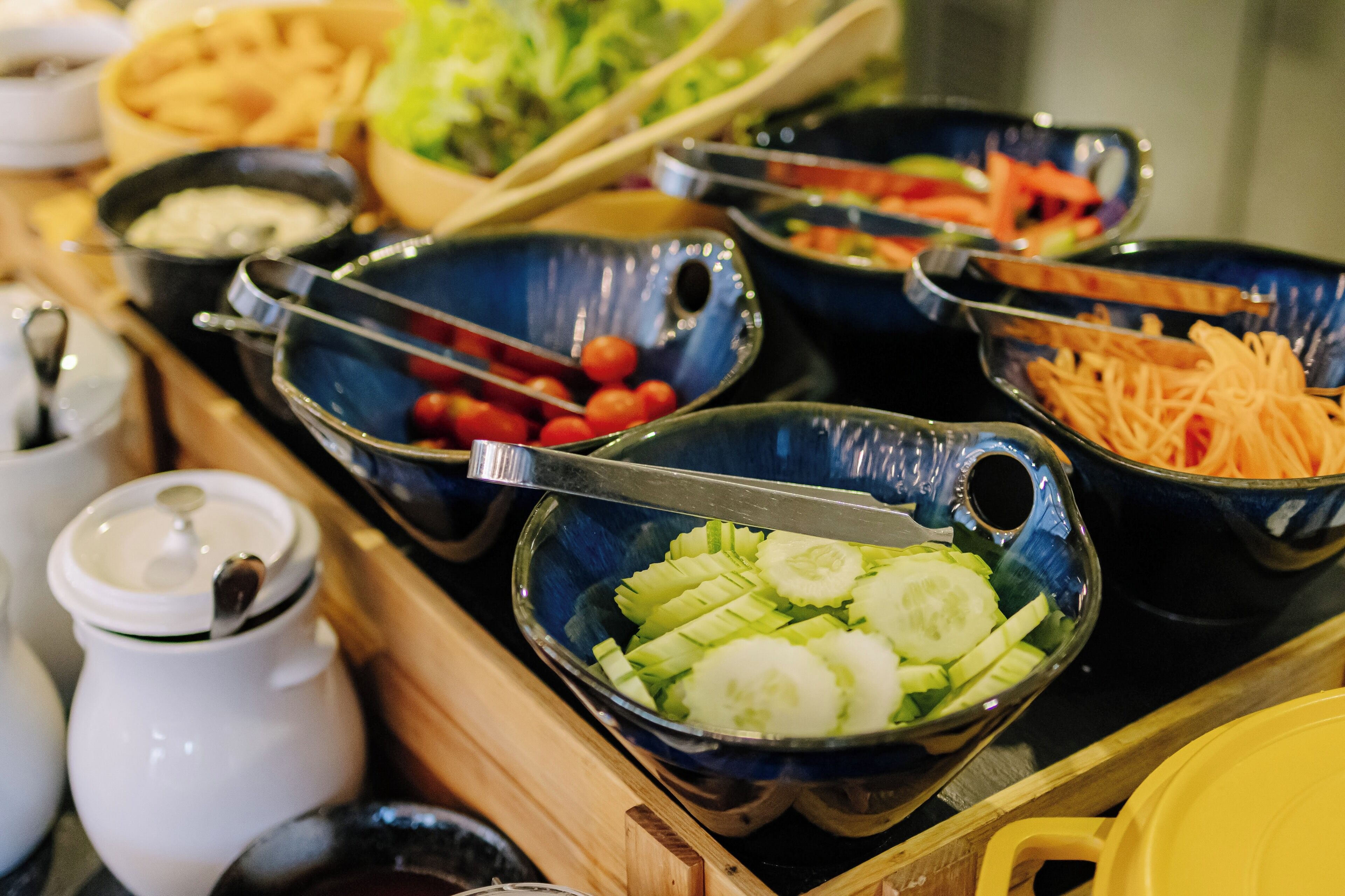 Ein Buffet mit verschiedenen Speisen, darunter Gurkenscheiben, Kirschtomaten und geriebene Karotten.