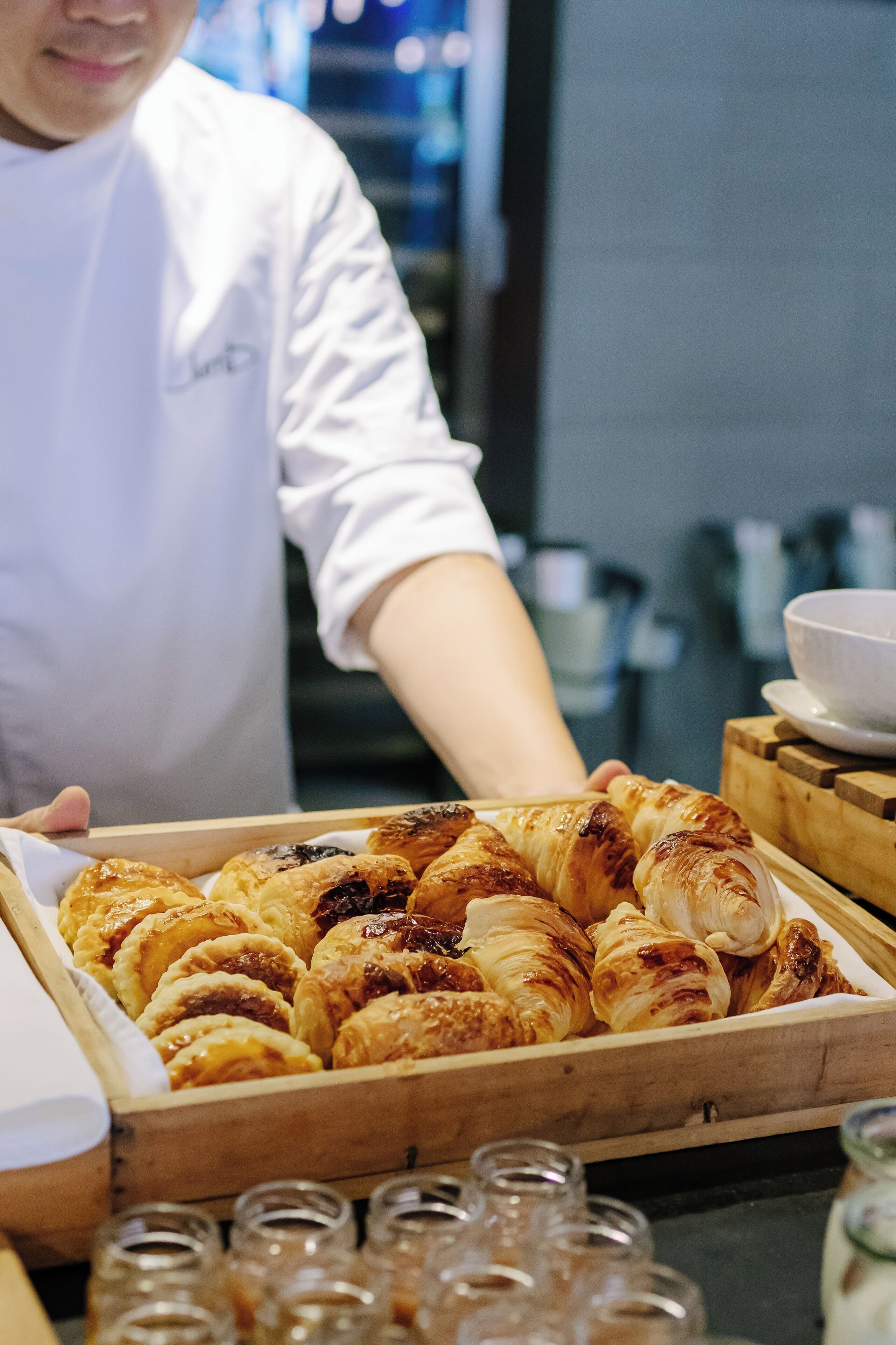A tray of assorted pastries, including croissants and tarts, being held by a person in a white uniform.
