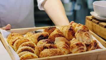 A tray of assorted pastries, including croissants and tarts, being held by a person in a white uniform.