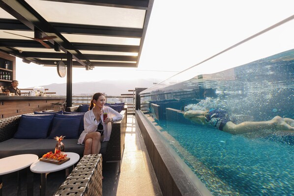 Uma área de piscina no terraço, com espaço para sentar, bar e vista para a piscina.