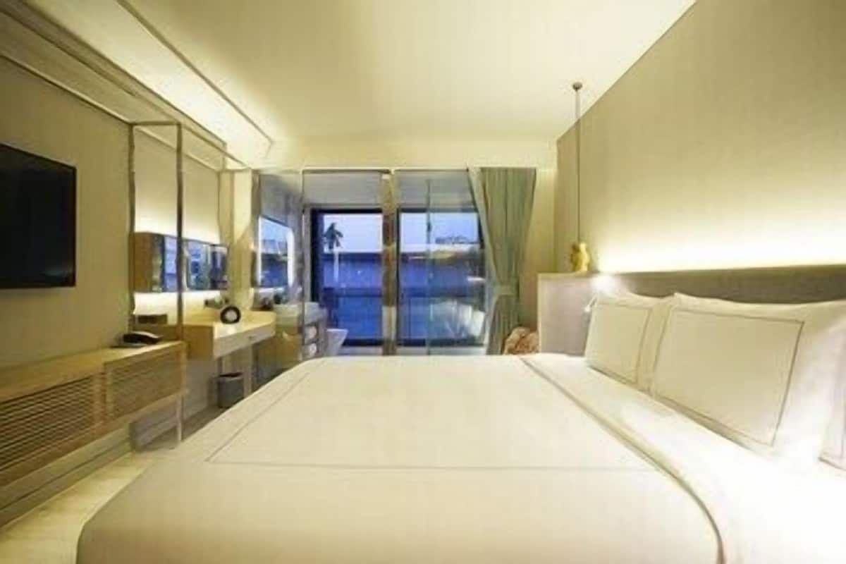 Ein Hotelzimmer mit einem großen Bett, einem an der Wand befestigten Fernseher, einem Schreibtisch mit Stuhl und Meerblick durch eine Glastür.