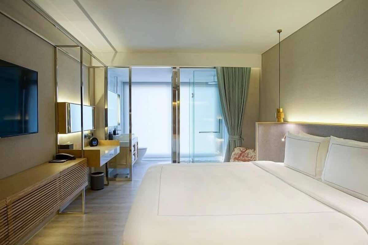 Ein modernes Hotelzimmer mit einem großen Bett, einem Schreibtisch, einem Spiegel und einem Fernseher.