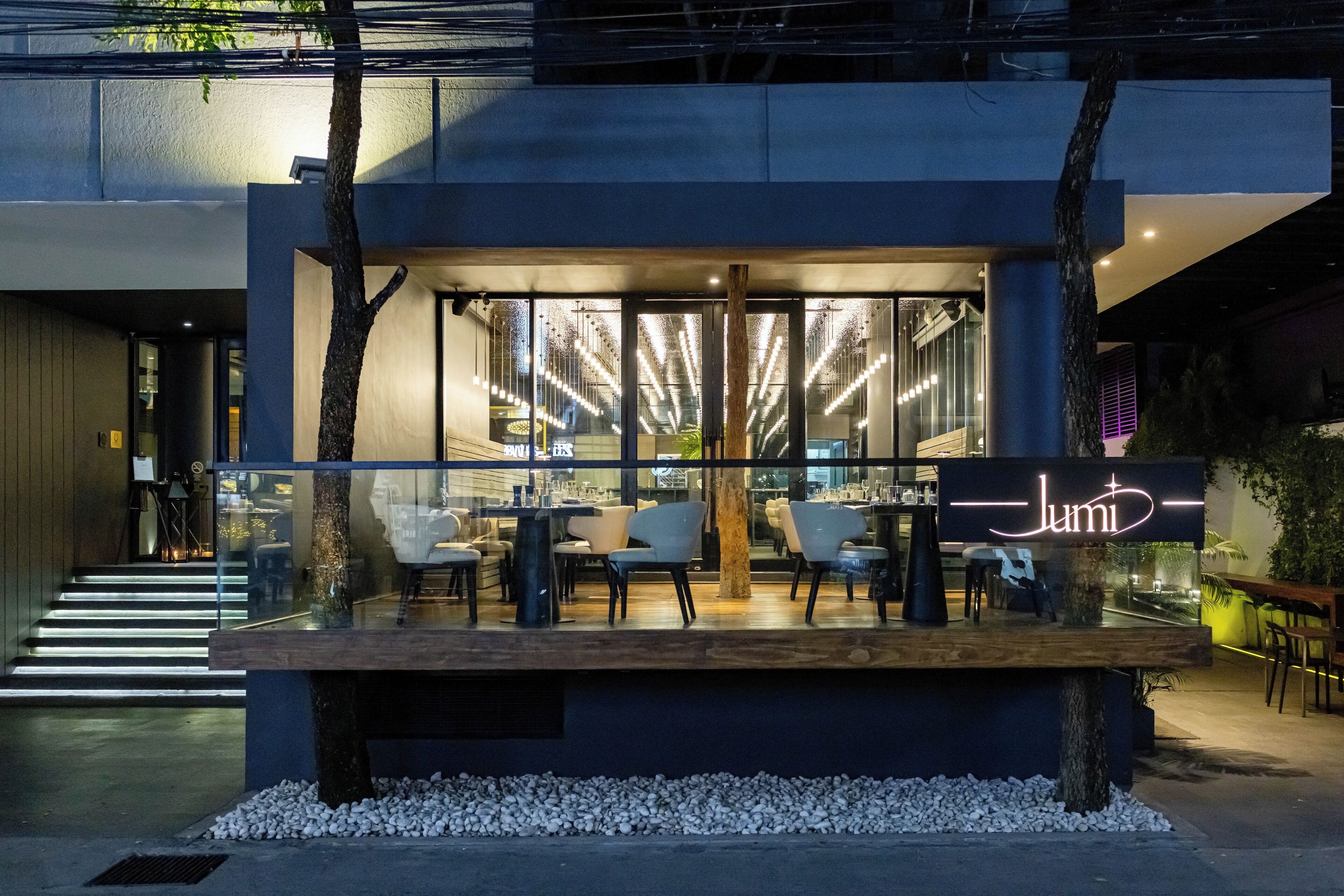 Un espacio moderno al aire libre con una señal de neón, puertas de vidrio y una escalera que lleva a la entrada.